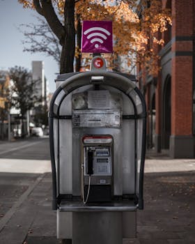 A vintage phone booth on a quiet street in Perth, framed by fall foliage.