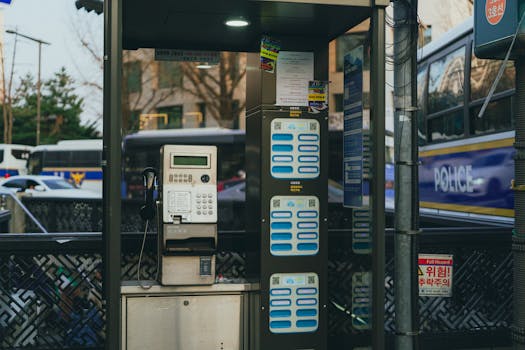 Classic payphone booth on a bustling Seoul street with buses in background, showcasing city life.