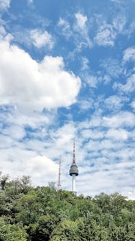 The iconic Namsan Tower in Seoul rises above a lush green landscape on a clear day with a picturesque sky.