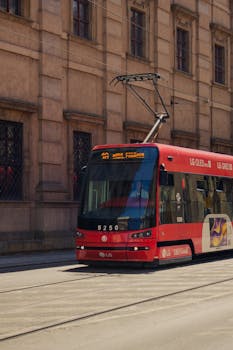 Red tram passing by a historic building on a sunny day, showcasing urban public transportation.