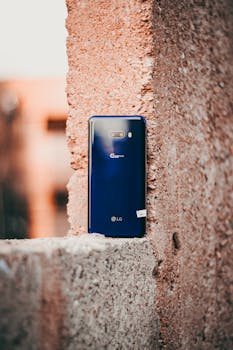 Blue LG smartphone with dual camera leaning against a rough concrete wall in an outdoor setting.