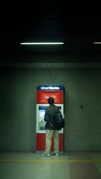Man using an ATM machine in a dimly lit indoor setting. Night urban scene.