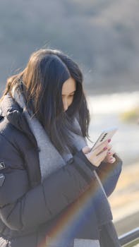 A woman in a warm coat checks her smartphone outdoors in Kyoto, Japan.