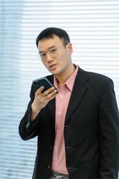 Asian businessman in suit using smartphone for communication in an office setting.